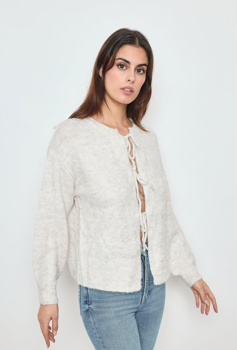 Model draagt een beige gebreide trui met strik, ideaal voor een comfortabele en modieuze outfit.