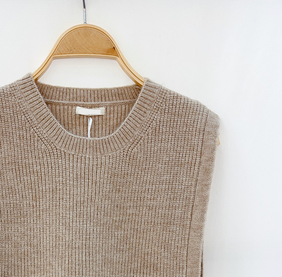 Close-up van de taupe gebreide top met subtiele ribstructuur en strikjes aan de zijkanten.
