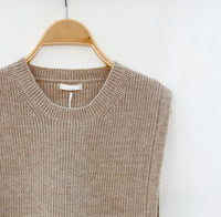 Close-up van de taupe gebreide top met subtiele ribstructuur en strikjes aan de zijkanten.
