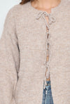 Detail van de strik op de taupe gebreide trui, een trendy en vrouwelijke touch voor een elegante uitstraling.