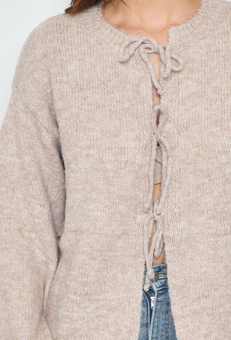 Detail van de strik op de taupe gebreide trui, een trendy en vrouwelijke touch voor een elegante uitstraling.