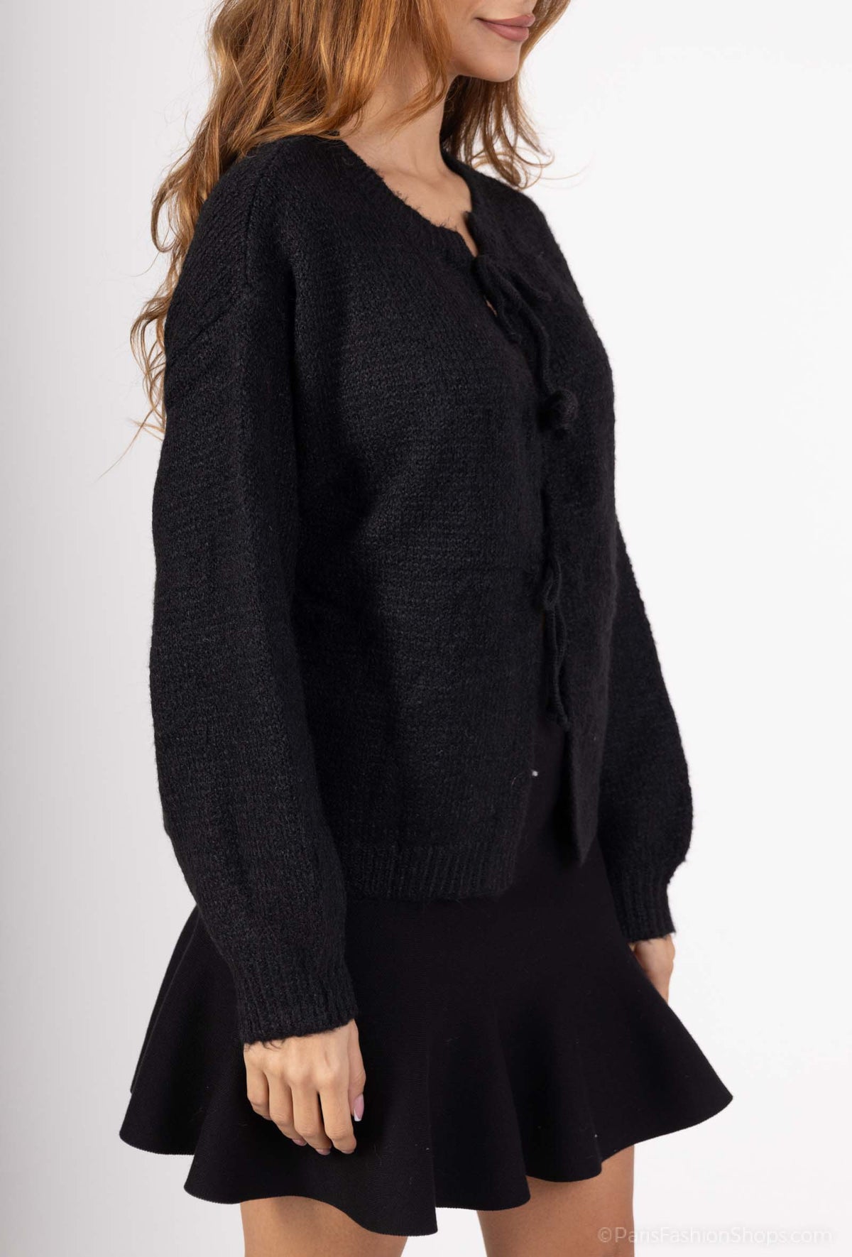 Model draagt een zwarte gebreide trui met strik, perfect voor een elegante en comfortabele outfit.