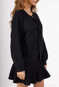 Model draagt een zwarte gebreide trui met strik, perfect voor een elegante en comfortabele outfit.